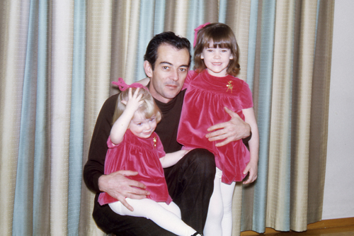 My sister and I, in matching Christmas dresses, posing with my dad