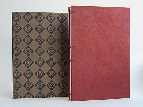 Two journals: one with copper spirals on a black checkerboard, one a solid red textured paper