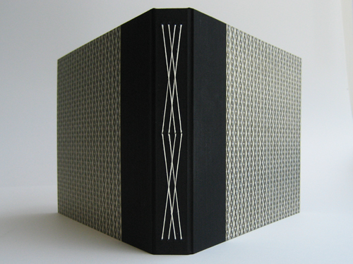 Spine view: black bookcloth spine with white stitching, with Japanese paper on the covers