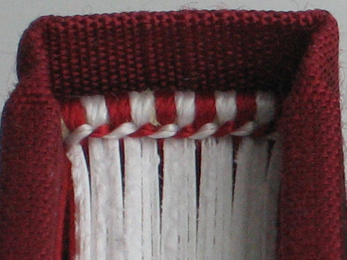 Endband with red and white stitching against red bookcloth and white pages.