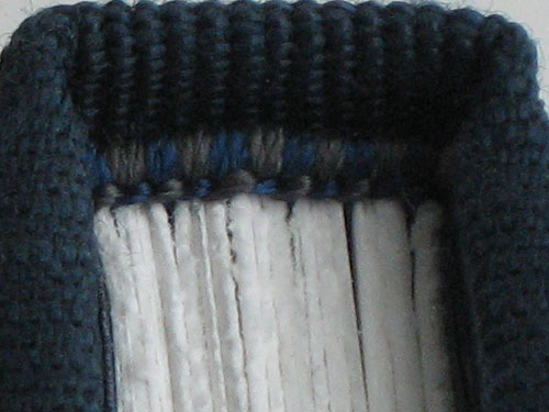 Endband with blue and gray stitching against blue bookcloth and white pages.