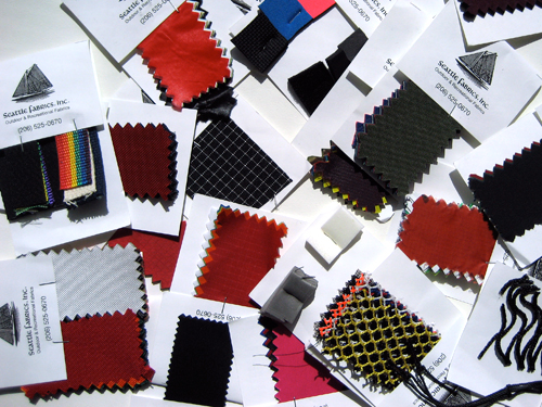 More than a dozen sample cards from Seattle Fabrics showing various colors and weights of nylon, cordura, netting, and foam