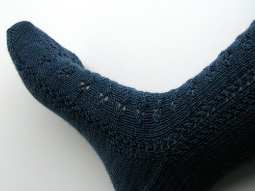 Side view of sock on foot, showing the heel gusset and the line of eyelets up the side.