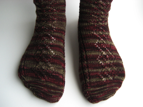 Lace and Cable Socks, front view; the yarn is self-striping in tones from burgundy to olive.