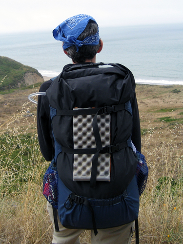 Back view of the fully packed backpack on my back, with a seating pad anchored by horizontal straps