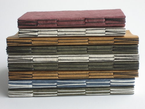 Stack of long stitch journals in assorted colors, with the spine stitching showing