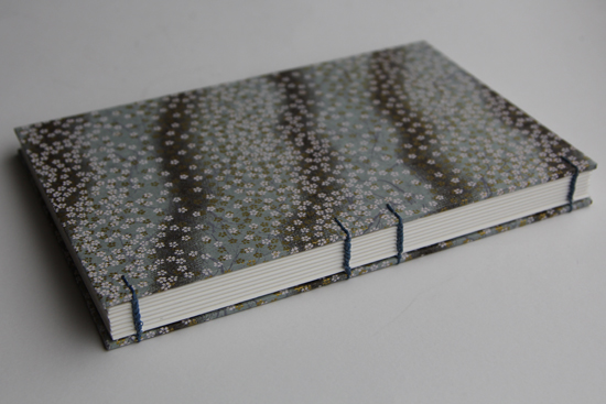 White blossoms on blue and gray patterned paper with light blue Coptic stitch on spine
